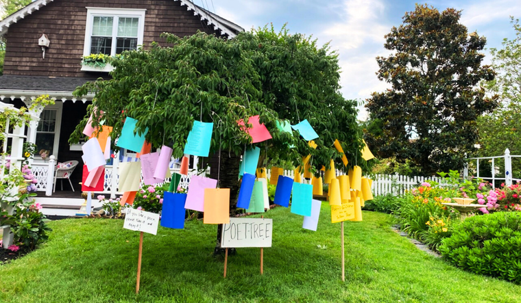 A tree in the front yard holds dozens of colorful papers tied to strings.